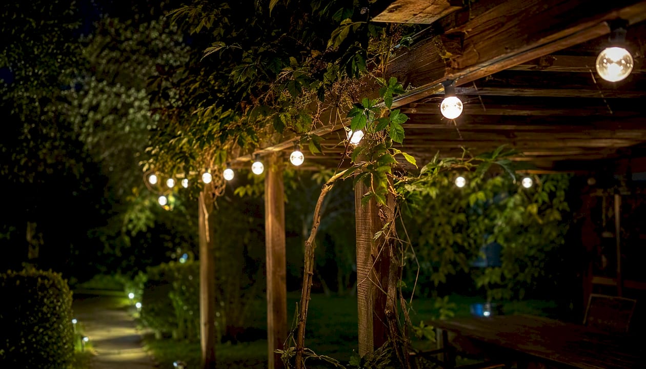Pergola w ogrodzie ozdobiona girlandami solarnymi to świetny sposób na stworzenie przytulnej atmosfery podczas letnich wieczorów.