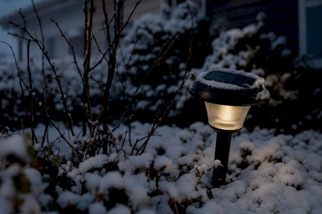 Lampa solarna słabo świecąca o zmierzchu w zimowym ogrodzie